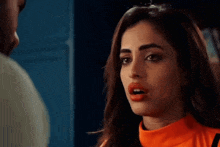 a woman in an orange shirt is looking at a man in a blue shirt .