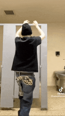 a man in a black shirt and jeans is standing in a bathroom stall