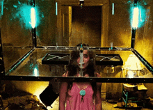 a woman in a pink shirt is standing in a glass box with a syringe in her face