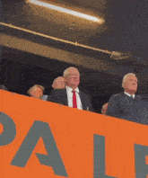 a man in a suit and tie stands in front of a large orange sign that says pale