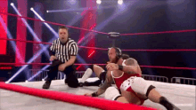 two men are wrestling in a ring with a referee in the background .