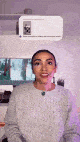 a woman wearing a grey sweater is standing in front of a tv screen .