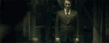a man in a suit and tie is standing in a dark hallway holding a knife .