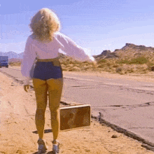 a woman is walking down a dirt road with a suitcase in her hand .