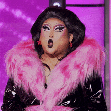 a drag queen wearing a pink fur coat is making a surprised face