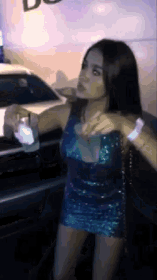 a woman in a blue sequined dress is standing in front of a car