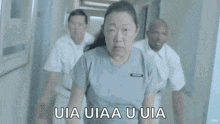 a woman in a hospital gown is running down a hallway with two men behind her .