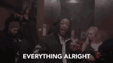 a man is standing in front of a crowd of people with the words `` everything alright '' above him .