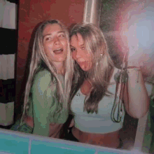 two women are posing for a picture together in front of a mirror .