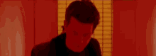 a man in a black shirt is standing in front of a window in a red room .