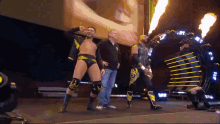 a group of wrestlers are walking on a stage with a man standing behind them