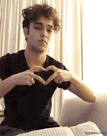 a young man in a black shirt is making a heart shape with his hands