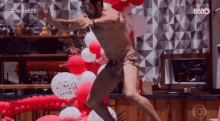 a shirtless man is jumping in the air in front of balloons and a wall .