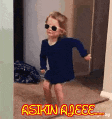 a little girl wearing sunglasses and a blue dress is dancing in a hallway .