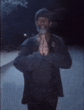a man with a beard is standing in the dark with his hands together in a prayer position .