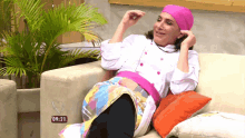 a woman in a pink hat sits on a couch with a clock reading 09:21