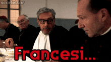 a man with glasses sits at a table with the word francesi written in red