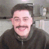a man with a mustache is smiling in front of a kitchen