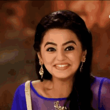 a woman wearing a purple top and earrings is smiling .