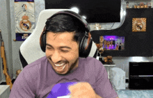 a man wearing headphones laughs in front of a real madrid poster