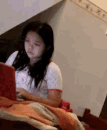 a young girl is sitting on a bed using a laptop