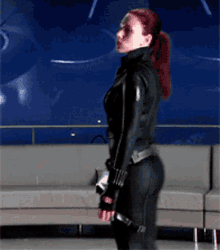 a woman in a black suit is standing in front of a grey couch