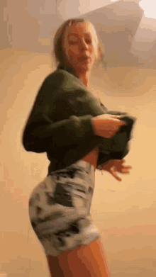 a woman in a green sweater and shorts is standing in a room .