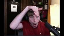 a man wearing headphones and a red shirt is making a face in front of a microphone
