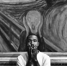 a black and white photo of a man covering his face in front of a painting of a scream