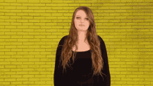 a woman in front of a yellow brick wall