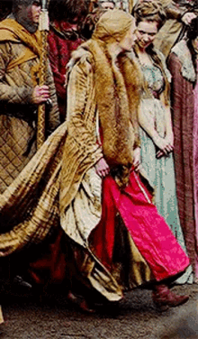 a woman in a red dress and a fur coat is walking in a crowd of people .