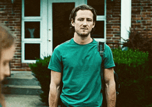 a man in a green shirt with a backpack stands in front of a brick building