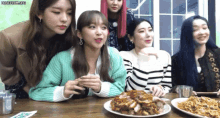 a group of girls sitting around a table with plates of food