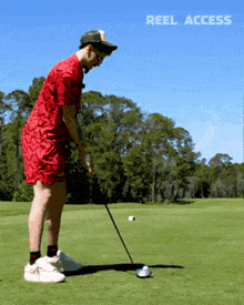 a man in a red shirt is swinging a golf club on a golf course with the words reel access behind him