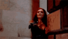 a woman with red hair is standing next to a brick wall in a dark room .
