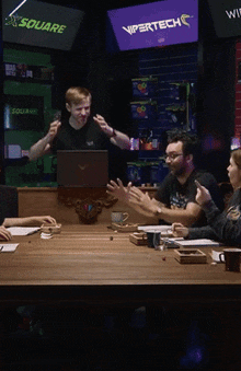 a group of people are sitting around a table with a vipertech sign behind them