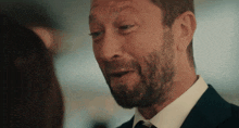 a man with a beard wearing a suit and tie looks at a woman