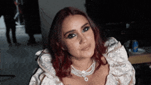 a woman with red hair wearing a white dress and pearls