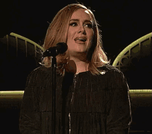 a woman in a black jacket is singing into a microphone on a stage .