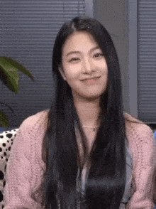 a woman with long black hair is wearing a pink sweater and a necklace .