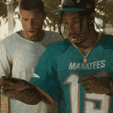 a man wearing a blue manatees jersey looks at his phone