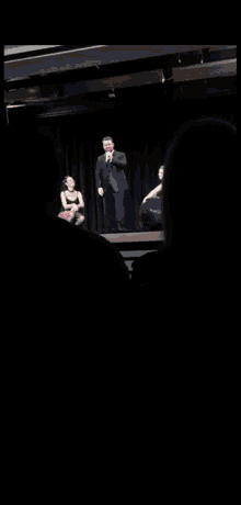 a man in a suit sits on a stage next to two women