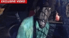 a man in a green shirt is sitting in a car with a red sign that says ' exclusive video ' on it
