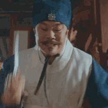 a man with a beard and mustache is wearing a blue hat and a white shirt .