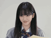 a girl in a school uniform is smiling while holding a book