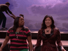 two women are holding hands on a stage and one has a necklace with a butterfly on it