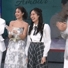 two women are standing next to each other and smiling while a man applauds .