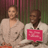 two women are sitting next to each other and one has a sign that says so true bestie