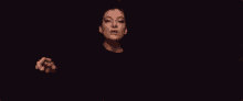 a woman in a black dress is standing in front of a crowd of people in a dark room .
