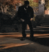 a man in a black jacket and sunglasses is dancing in front of stairs .